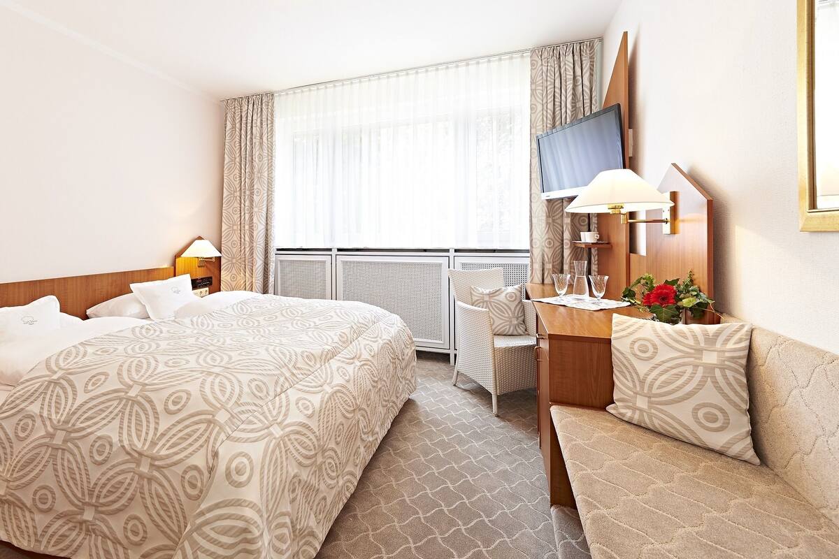 A hotel room with a large bed, a desk with a chair, a TV, and a window with curtains.