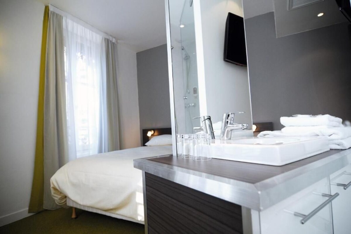 A hotel room with a bed, a bathroom with a sink and mirror, and a shower.