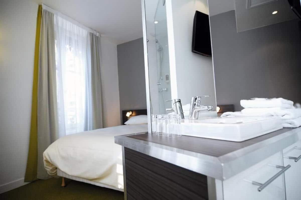 A hotel room with a bed, a bathroom with a sink and mirror, and a shower.