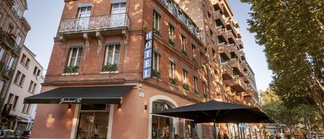 A hotel with a classic facade, large windows, and a balcony with ornate railings.