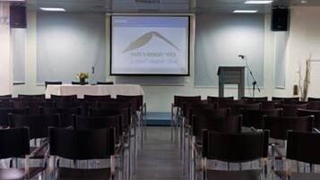 Un salón de conferencias con filas de sillas orientadas hacia una pantalla que muestra un gráfico.