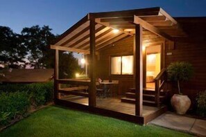 A wooden cabin with a covered porch, a staircase leading to the main entrance, and a large window. - Ramot Resort Hotel (Ramot)
