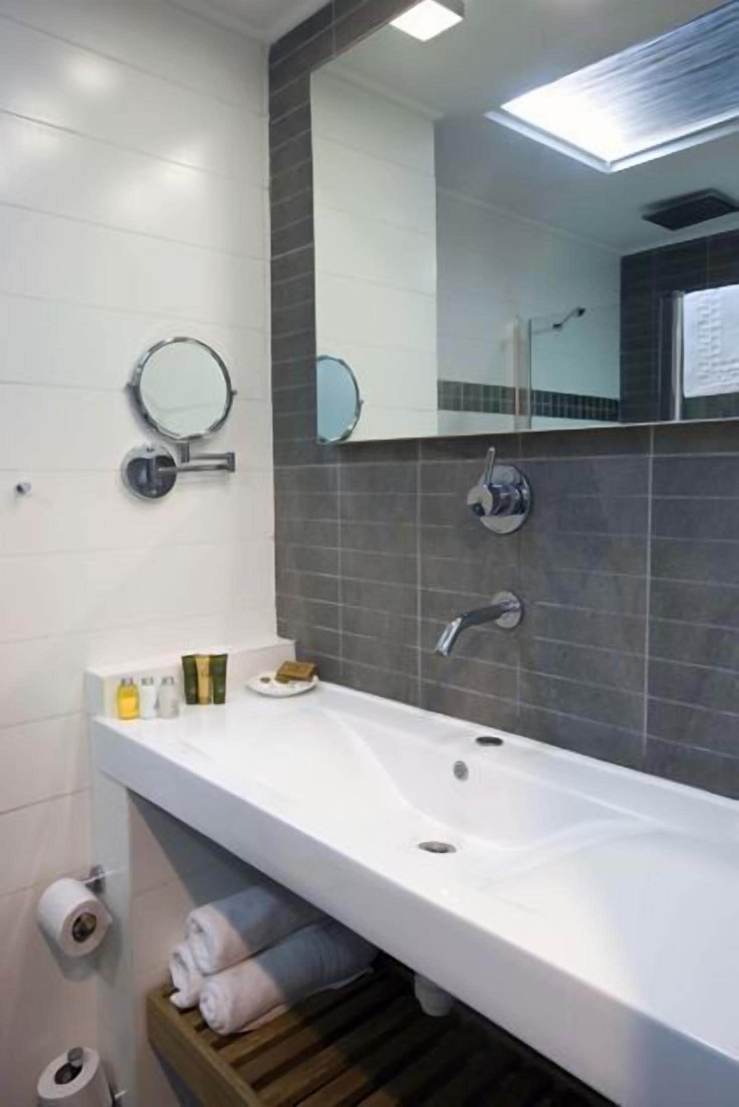 A modern bathroom with a long white sink, two mirrors, a towel rack, and a shower area.