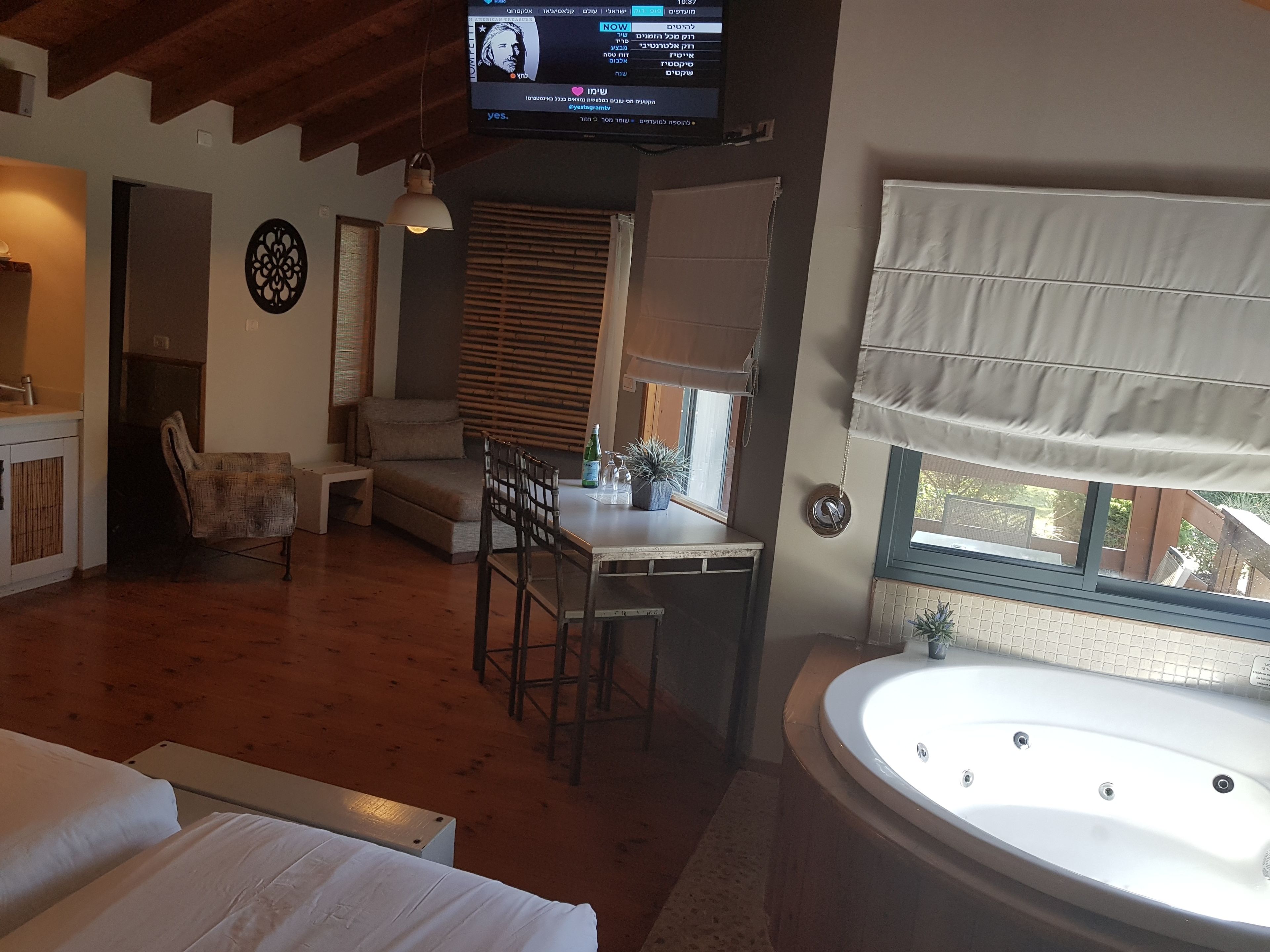 Una habitación acogedora con piso de madera, un sofá, una mesa de comedor con sillas, un televisor montado en la pared y una bañera grande.