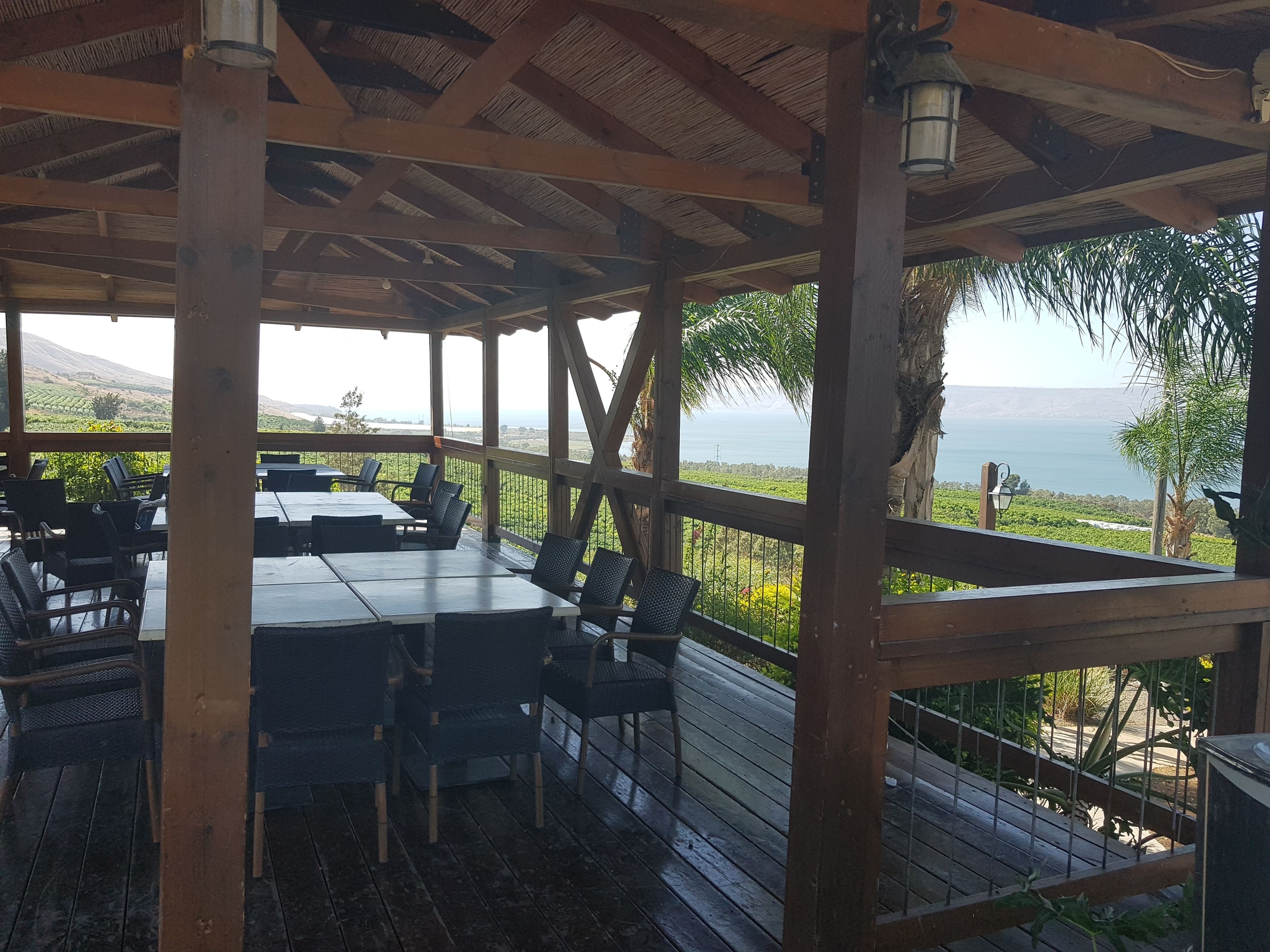 A covered outdoor seating area with tables and chairs, overlooking a scenic landscape with mountains and a body of water.