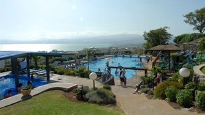 A pool area with a view of the sea, surrounded by lounge chairs and umbrellas. - Ramot Resort Hotel (Ramot)