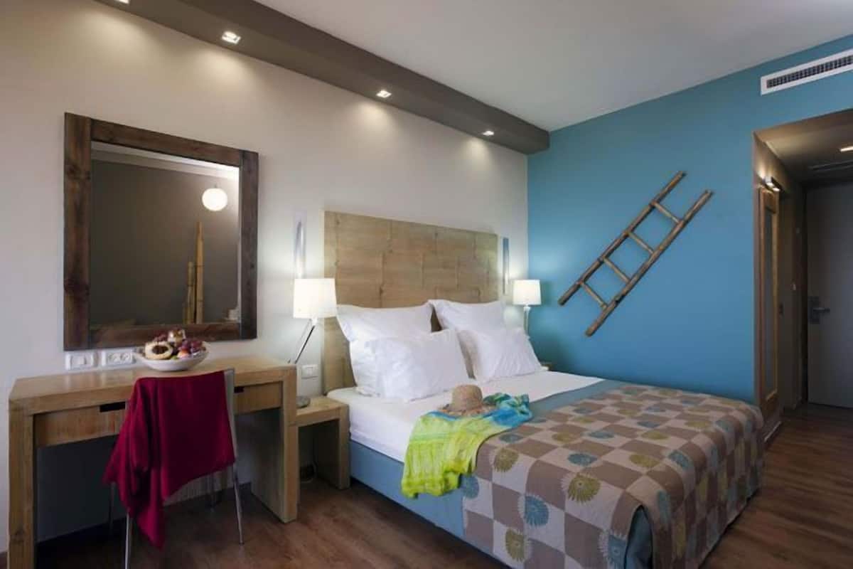A hotel room with a bed, bedside tables, a desk, a mirror, and a wall-mounted ladder.