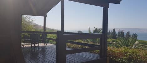 A wooden deck with a pergola, overlooking a coastal landscape with greenery and distant hills.