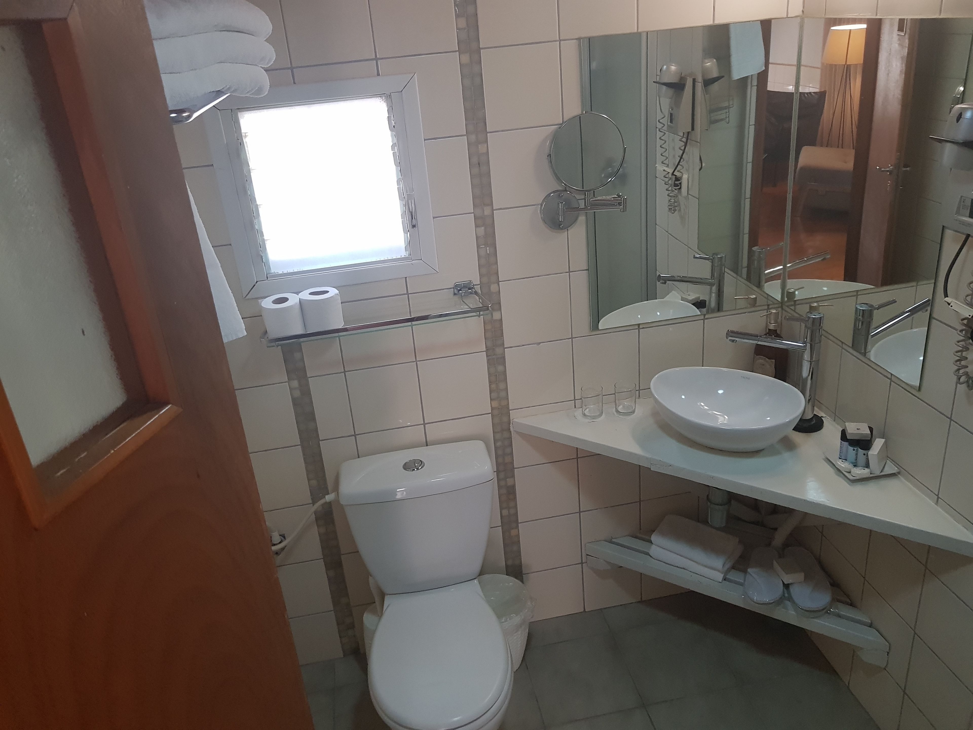 A bathroom with a toilet, sink, mirror, and a shelf with toiletries.