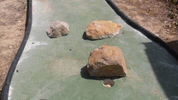 A green, curved pathway with rocks and a small pond.