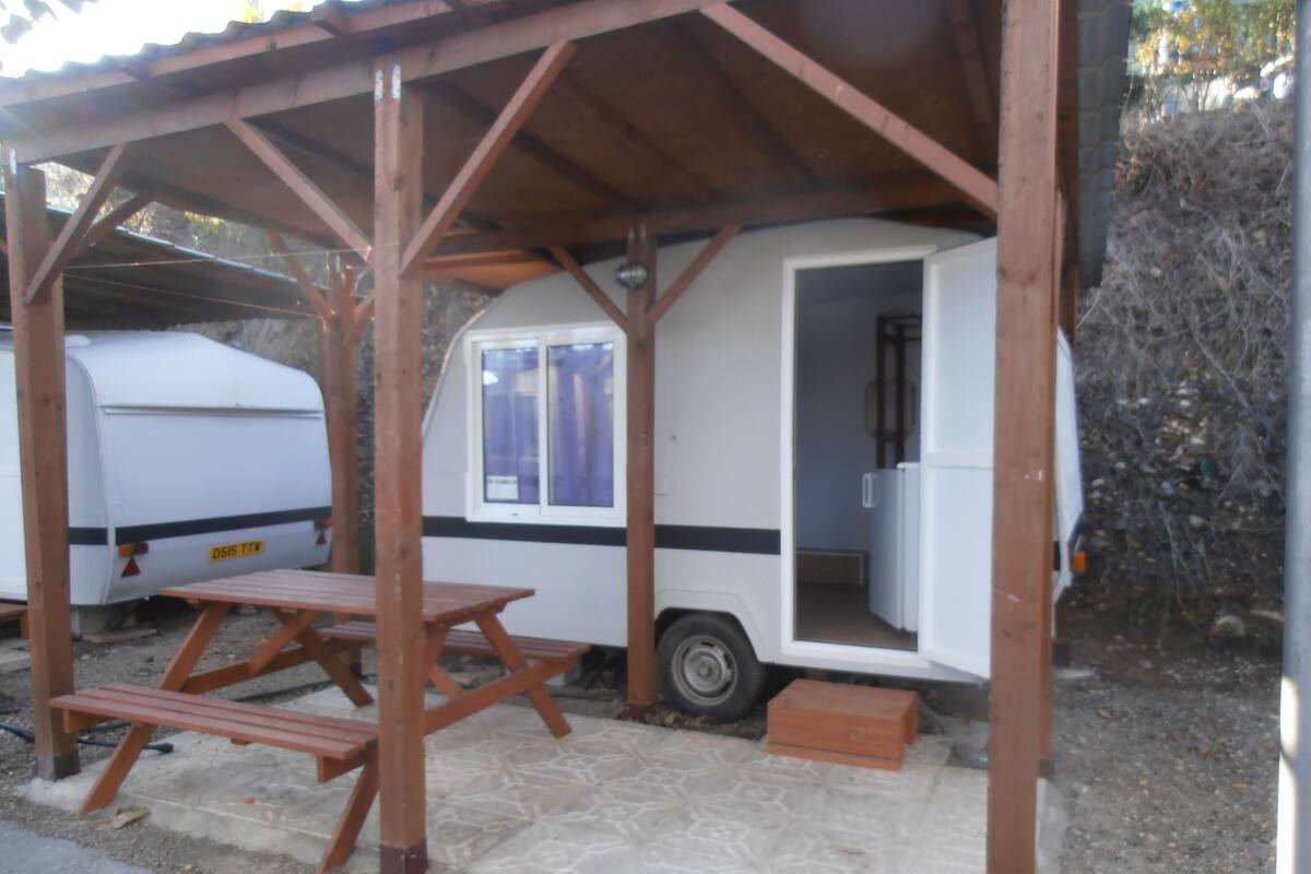 A caravan with a covered outdoor area, a picnic table, and a small enclosed space with a door.