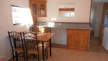 A compact kitchen with wooden cabinets, a dining table with chairs, and a small island.