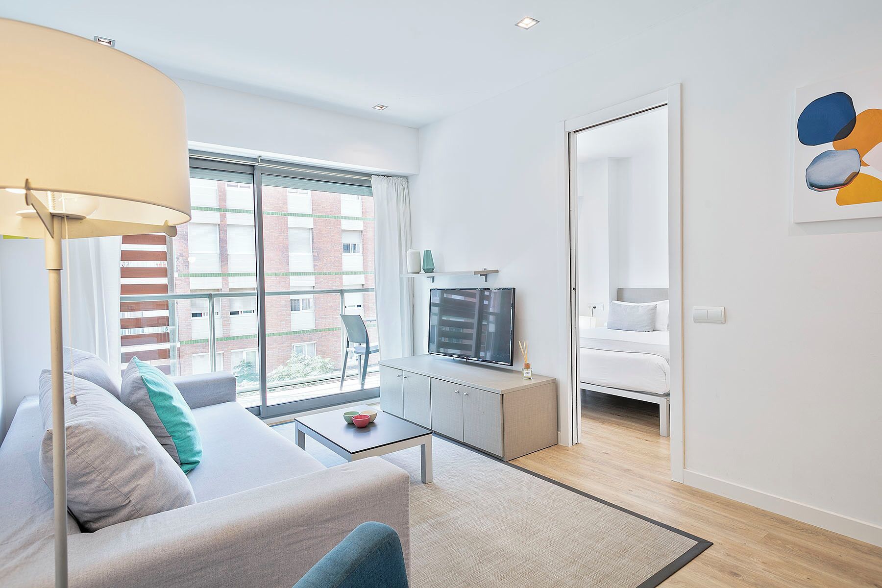 Un salon moderne avec un canapé, une table basse et un téléviseur. Il y a un balcon avec vue sur les immeubles.
