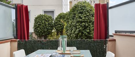 Un balcon avec une table en verre, des chaises blanches, un pichet en verre et un saladier.