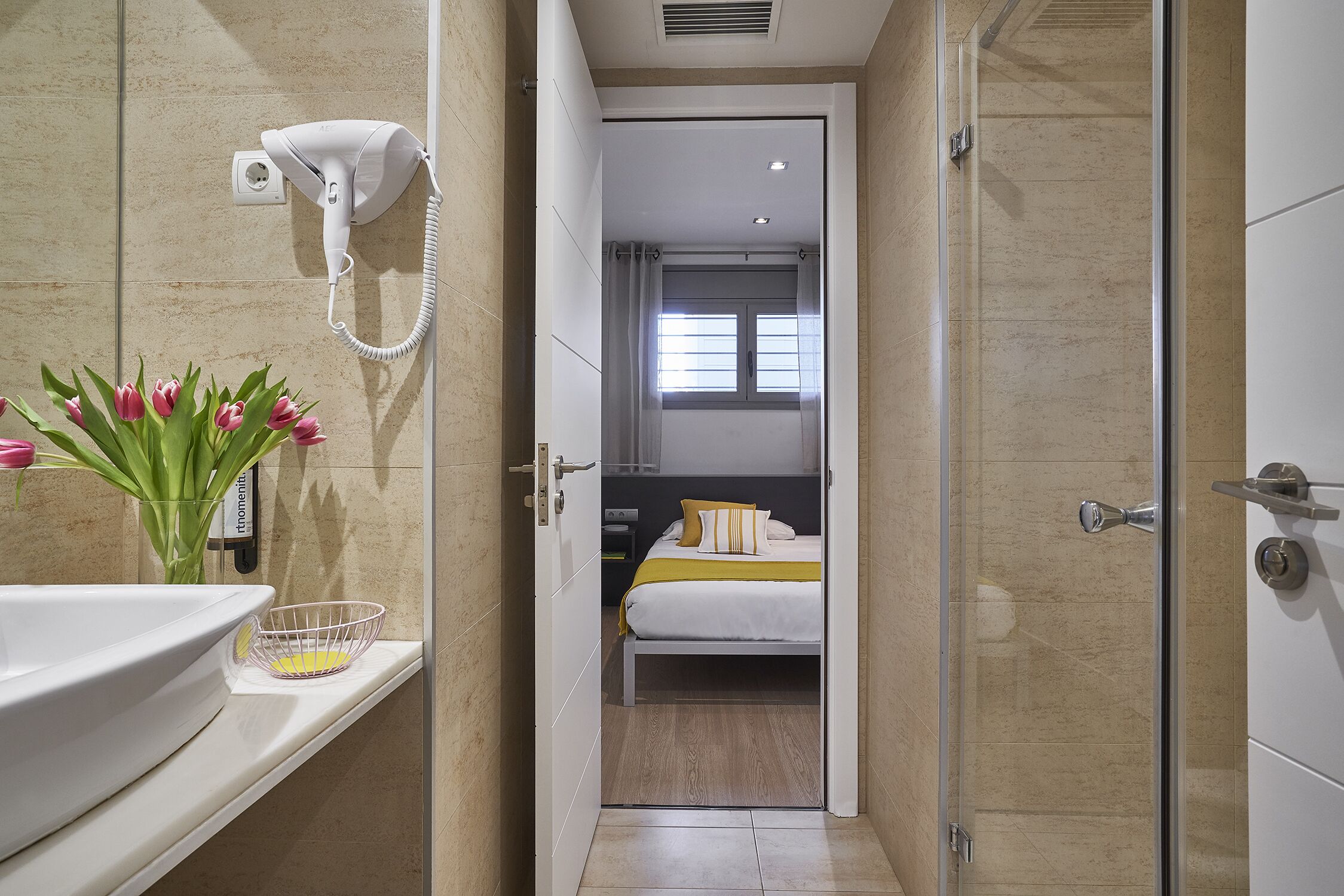 A hotel bathroom with a sink, a hairdryer mounted on the wall, and a shower area.