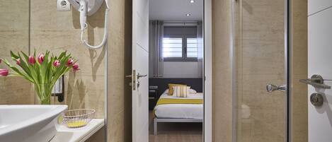 A hotel bathroom with a sink, a hairdryer mounted on the wall, and a shower area.
