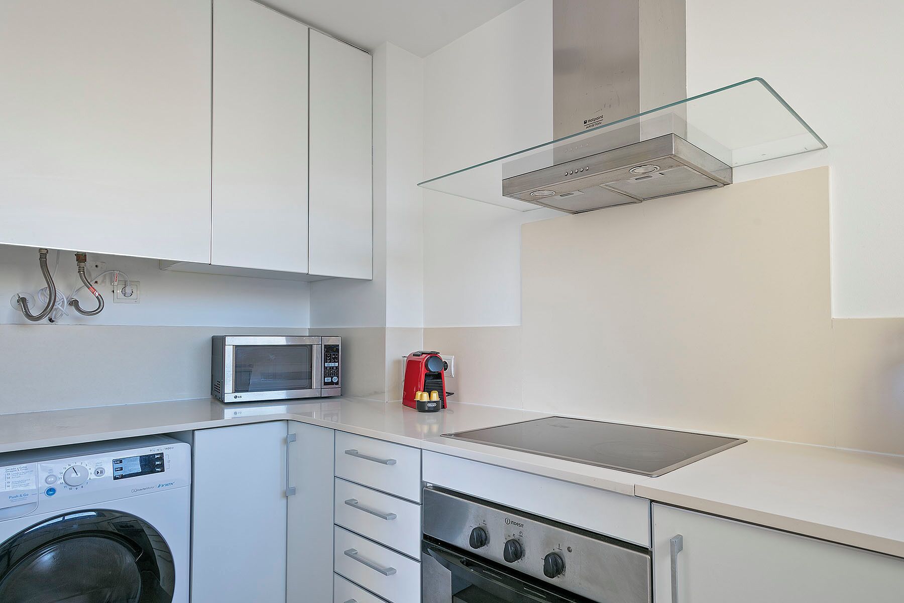 A compact kitchen with a washing machine, microwave, and stove.