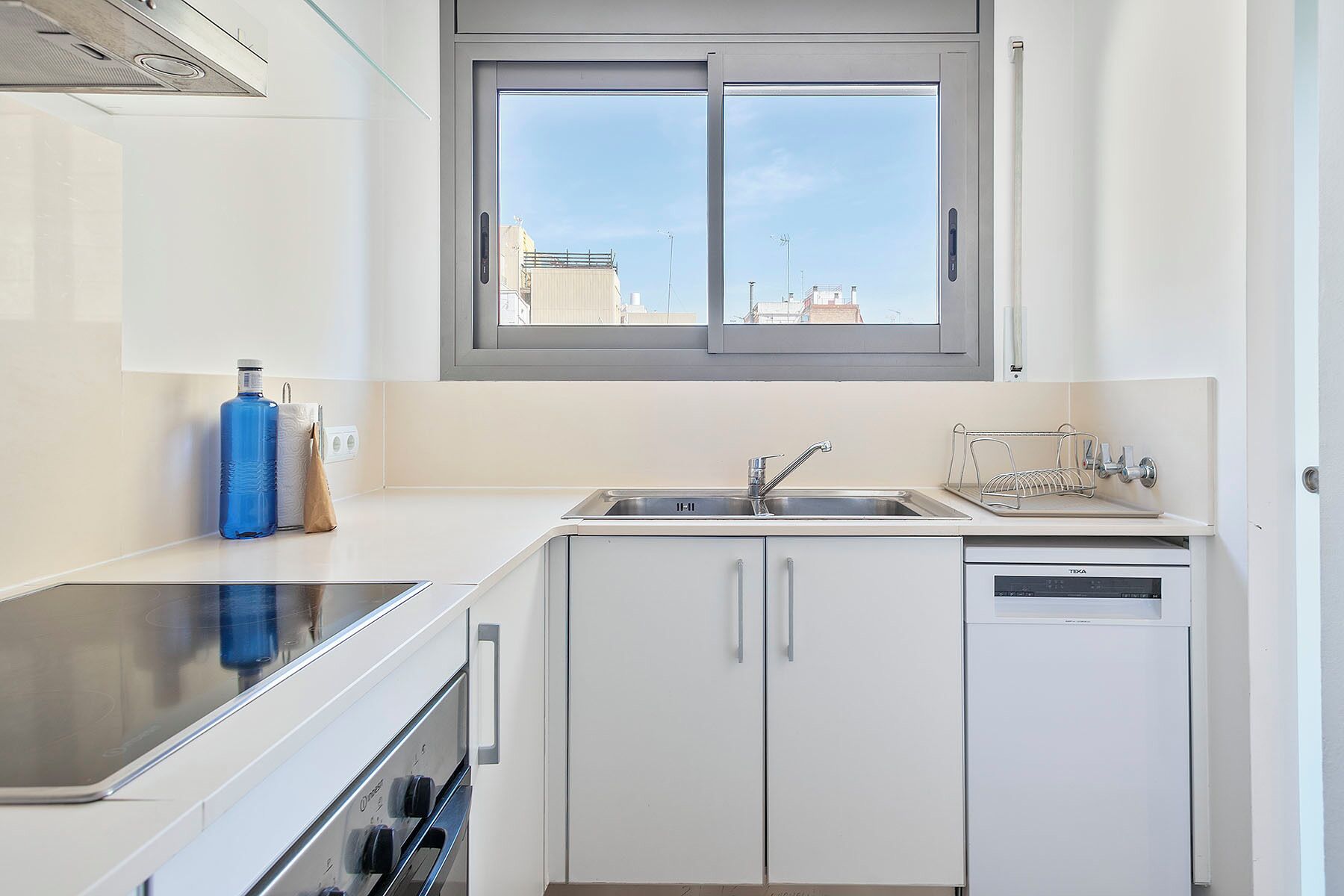 Una cocina moderna con armarios blancos, un lavamanos doble, horno empotrado y una ventana sobre el lavamanos.