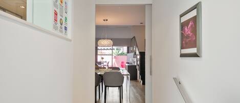 Un pasillo que conduce a un comedor con una mesa y sillas, un lámpara colgante y un cuadro en la pared.