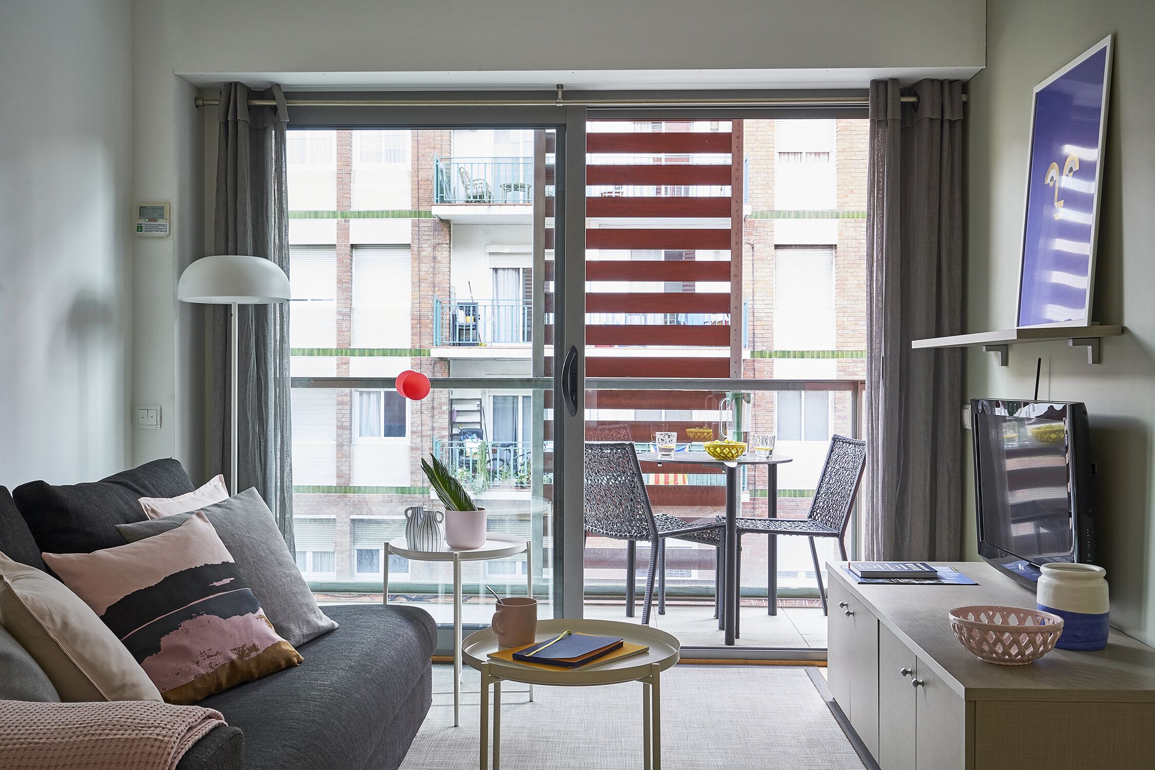 Un salon moderne avec un canapé, une petite table, un téléviseur et un balcon équipé d’une table et de chaises.