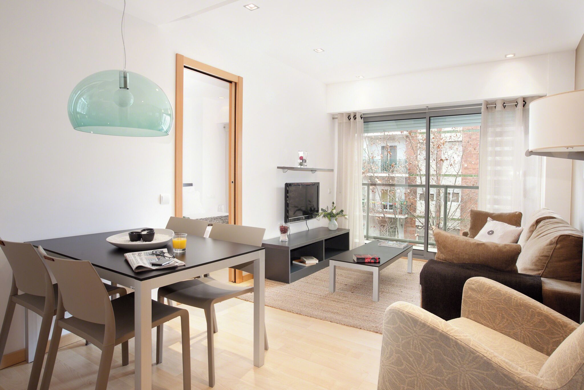 A modern living room with a dining area, a TV, and a large window with a view of buildings.