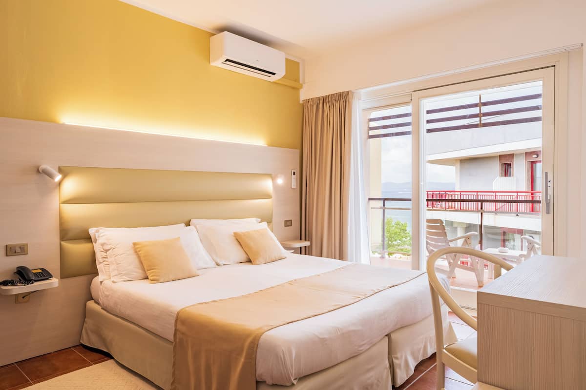 A hotel room with a large bed, bedside table, and a view of the balcony.