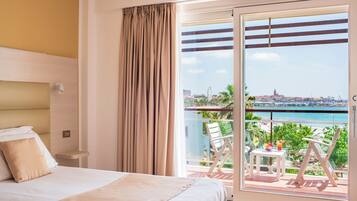 A hotel room with a bed, a balcony with a table and chairs, and a view of the city and sea.