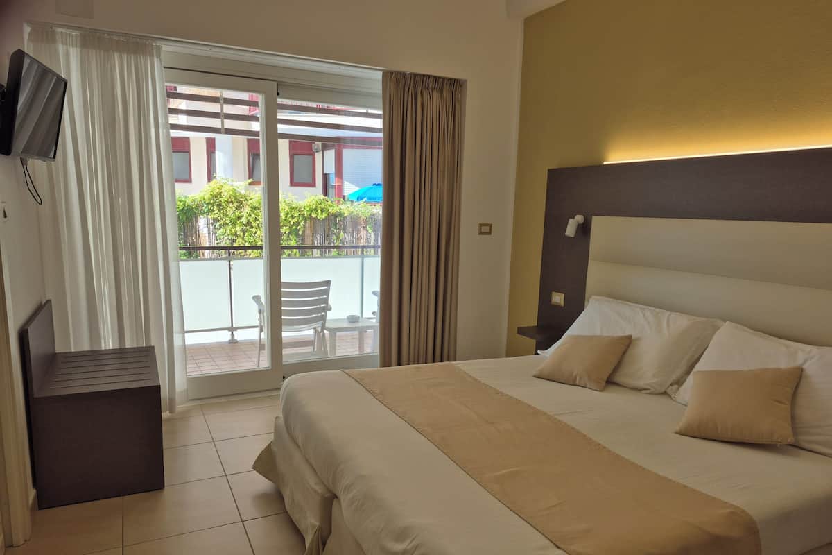 A hotel room with a bed, a TV, a desk, and a view of the outside balcony.