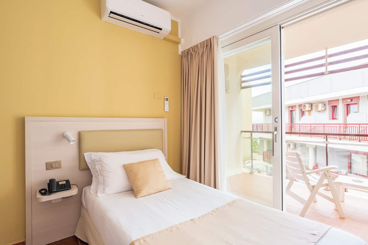 A hotel room with a bed, a bedside table, a phone, and a view of a balcony with outdoor furniture.