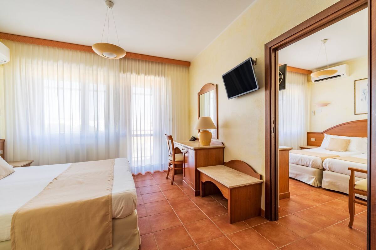 A hotel room with a bed, a desk, a chair, a TV, and a second bed.