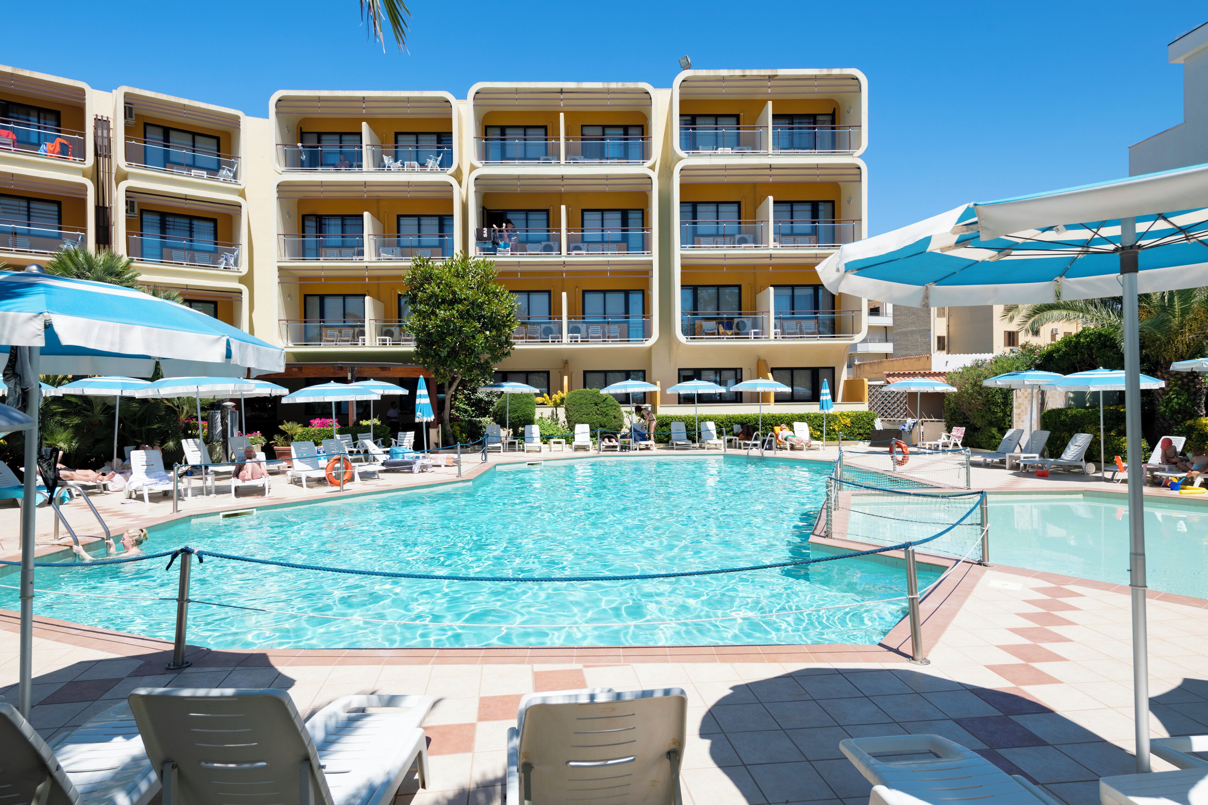 A hotel pool area with multiple levels of balconies, sun loungers, and umbrellas.