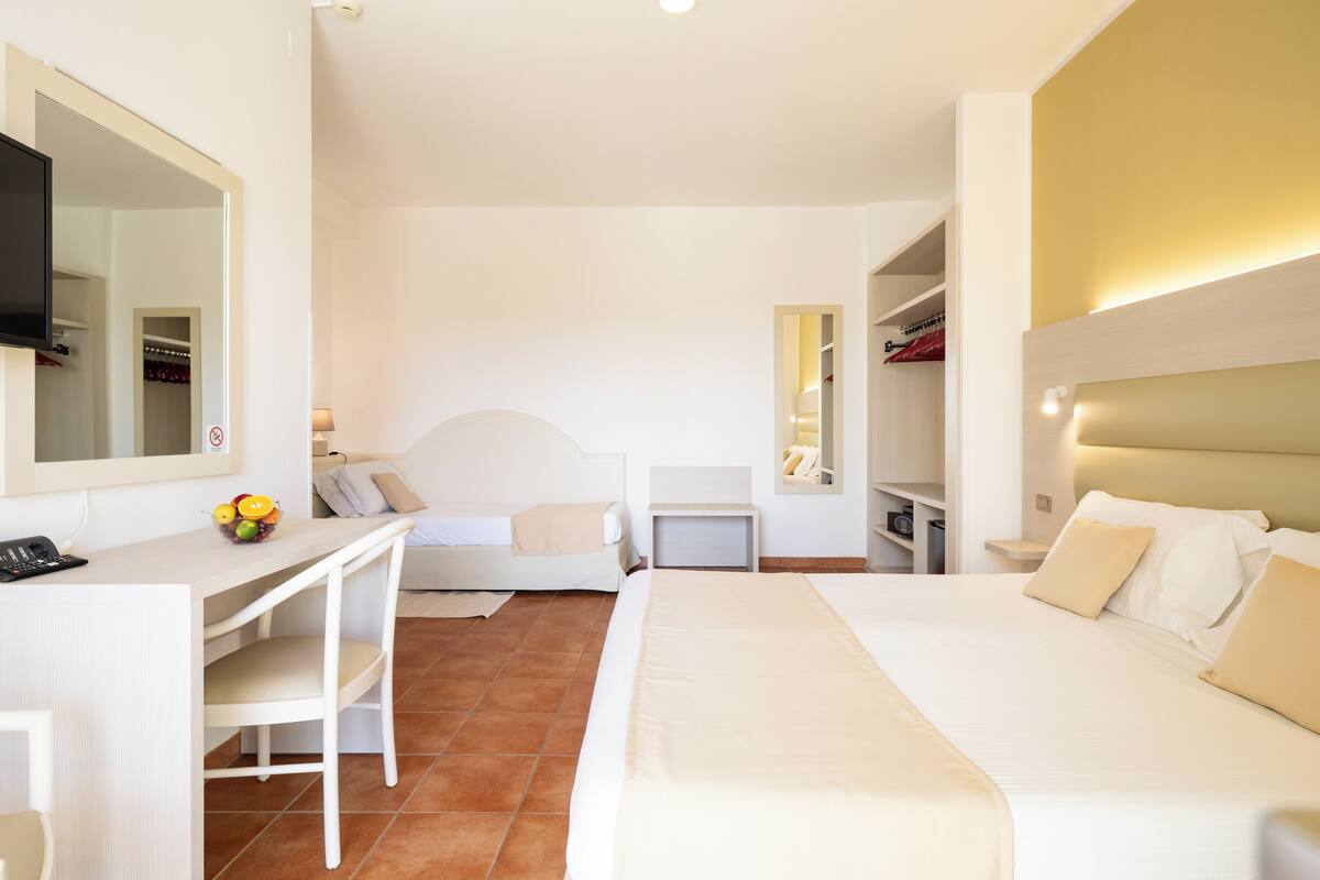 A hotel room with a bed, a desk, a chair, a TV, and a mirror.
