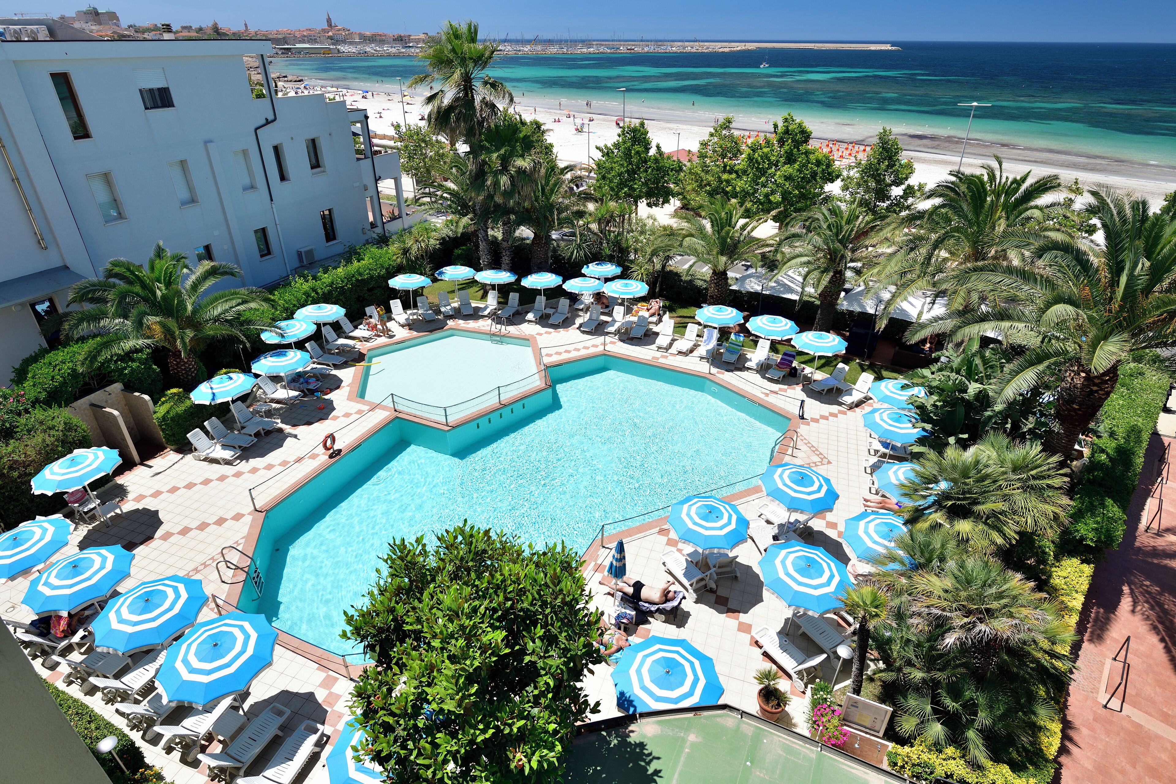 A pool area with lounge chairs and umbrellas, surrounded by palm trees and a view of the beach.