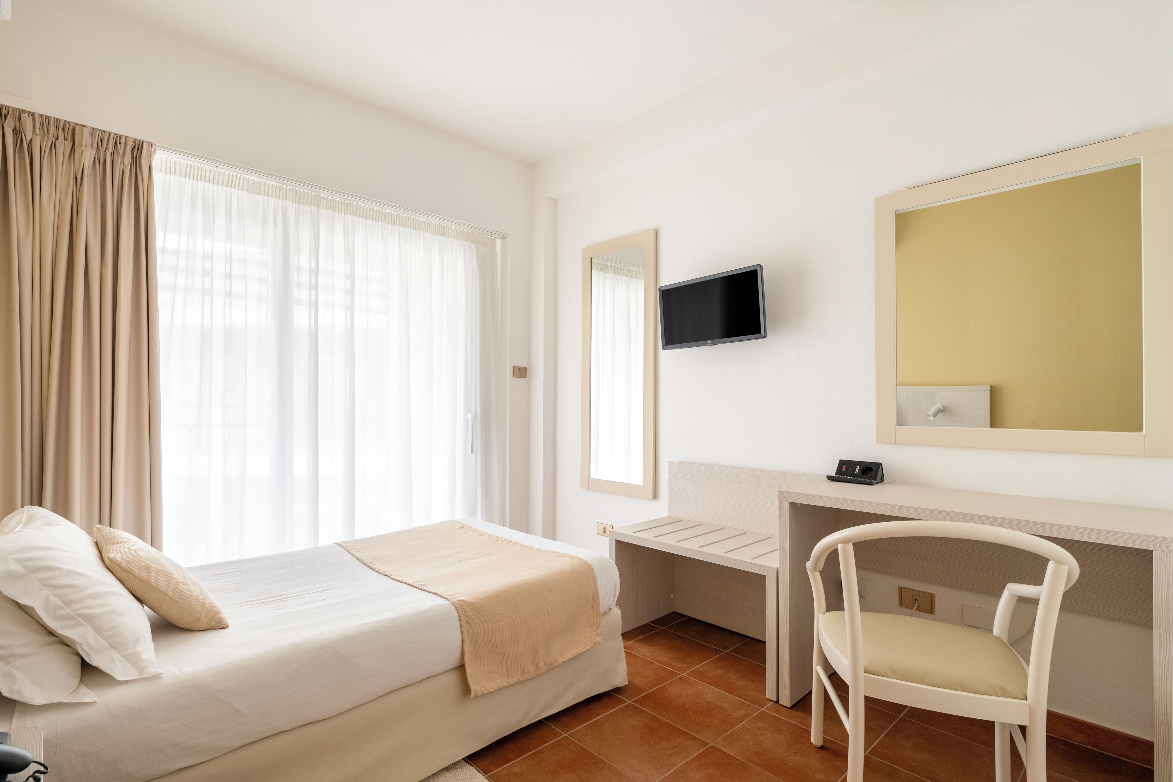 A bedroom with a bed, a desk, a chair, a TV, and a mirror.