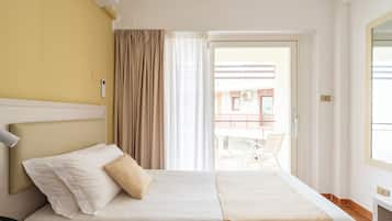 Una camera d'albergo con un letto, un comodino con una lampada, una finestra con tende e vista su un balcone esterno.