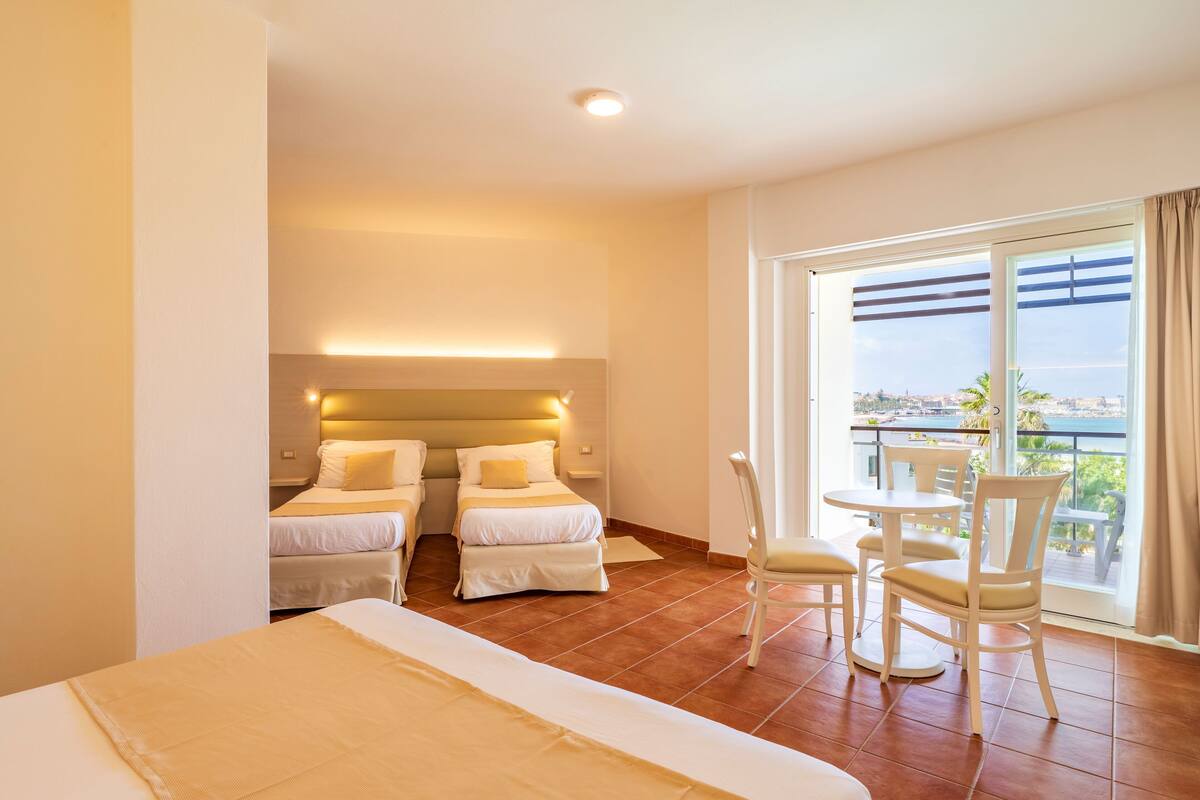 A hotel room with two beds, a balcony with a table and chairs, and a view of the city.