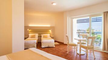 Habitación de hotel con dos camas, un balcón con mesa y sillas, y vista a la ciudad.