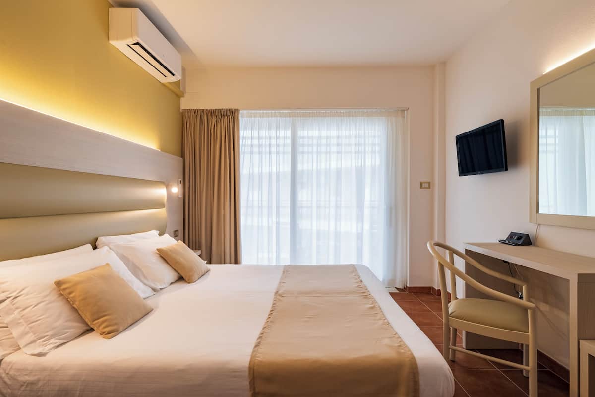 A hotel room with a large bed, a desk, a chair, a television, and a window with curtains.