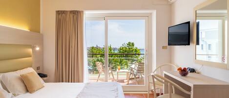 Quarto de hotel com cama, escrivaninha, cadeira, televisão e varanda com vista para a cidade.