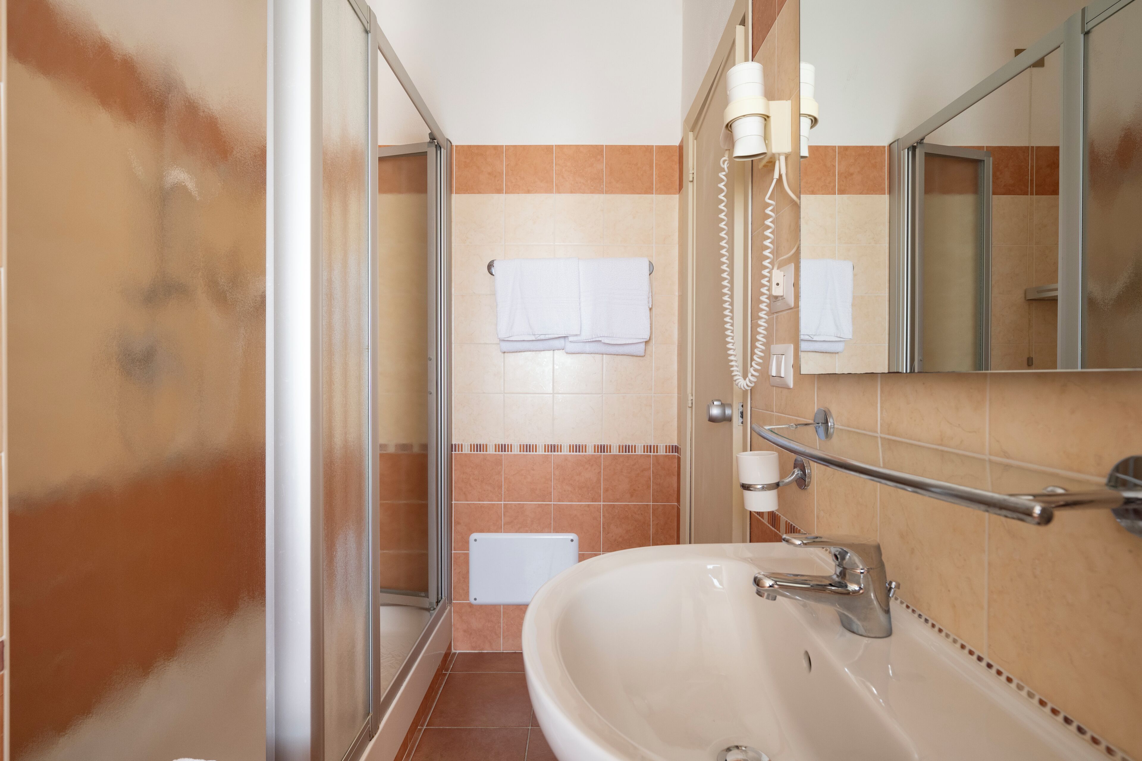 Un baño con bañera, ducha e inodoro. Hay un perchero con toallas y un secador de pelo en la pared.