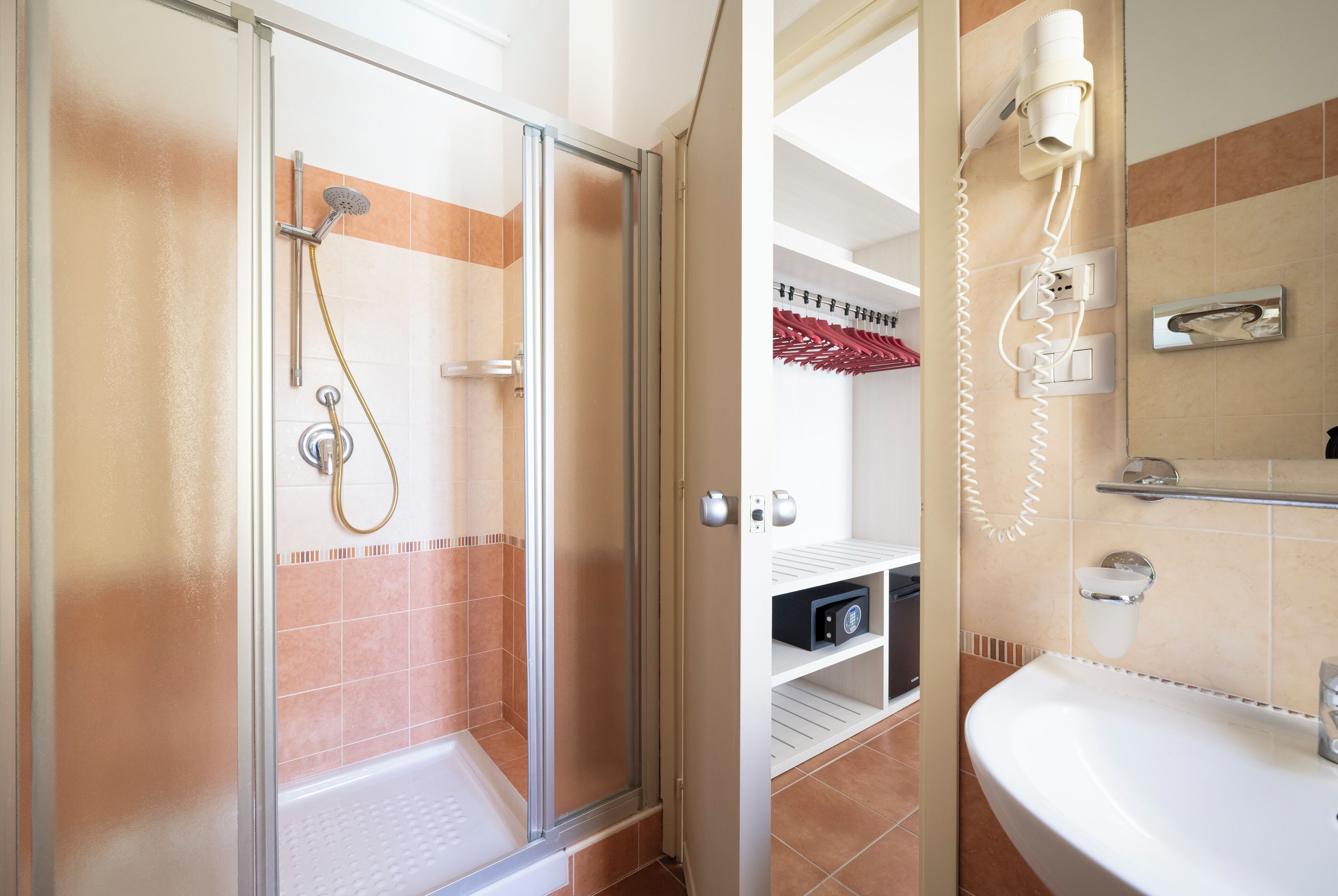 Un baño con ducha de vidrio, un lavamanos blanco y un secador de pelo montado en la pared.
