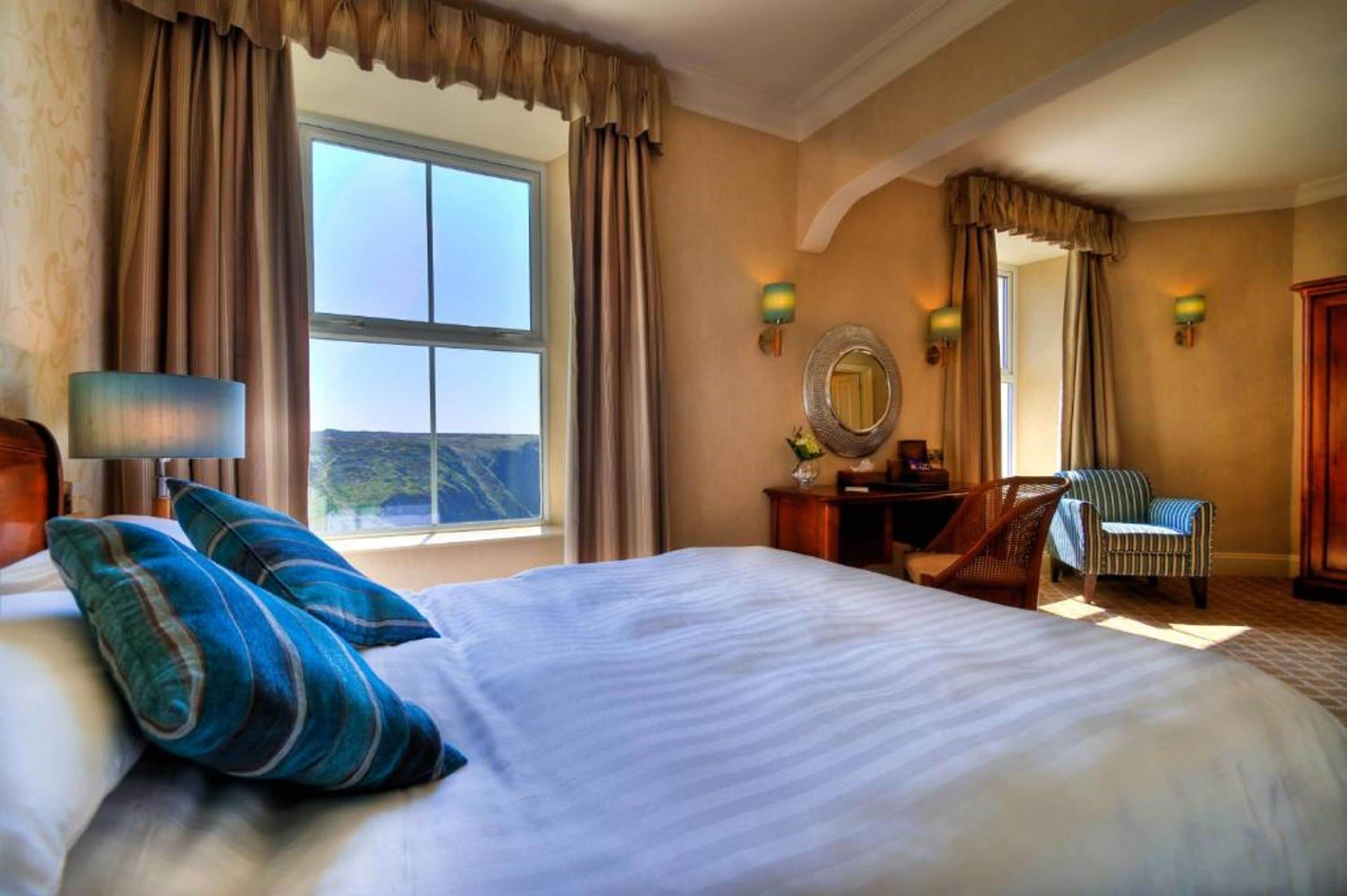 Una habitación de hotel con una cama grande, dos sillas, un escritorio y una ventana con cortinas.
