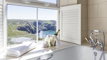 A bathroom with a bathtub, a shower, and a window with a view of a mountainous landscape.