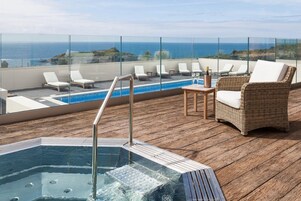 Un área de piscina en la azotea con sillones de descanso, un jacuzzi y vistas al océano.
