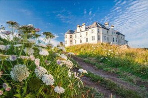 A large, white building with multiple chimneys, situated on a grassy hill with a clear sky. - Mullion Cove Hotel & Spa (Helston)