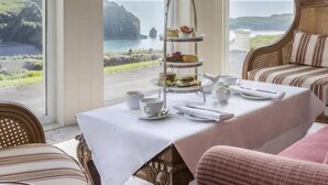 A dining area with a table set for tea service, overlooking a coastal landscape.