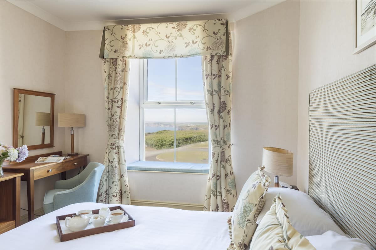 A hotel room with a bed, a desk, a chair, a window with curtains, and a view of the landscape.