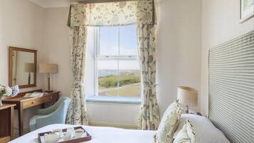 A hotel room with a bed, a desk, a chair, a window with curtains, and a view of the landscape.