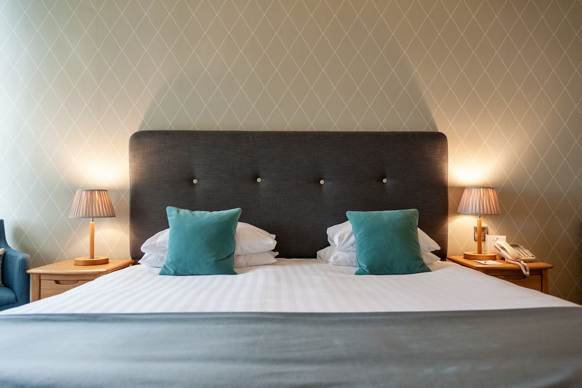 A hotel room with a large bed, two bedside tables, a lamp on each table, and a telephone on one of the tables.