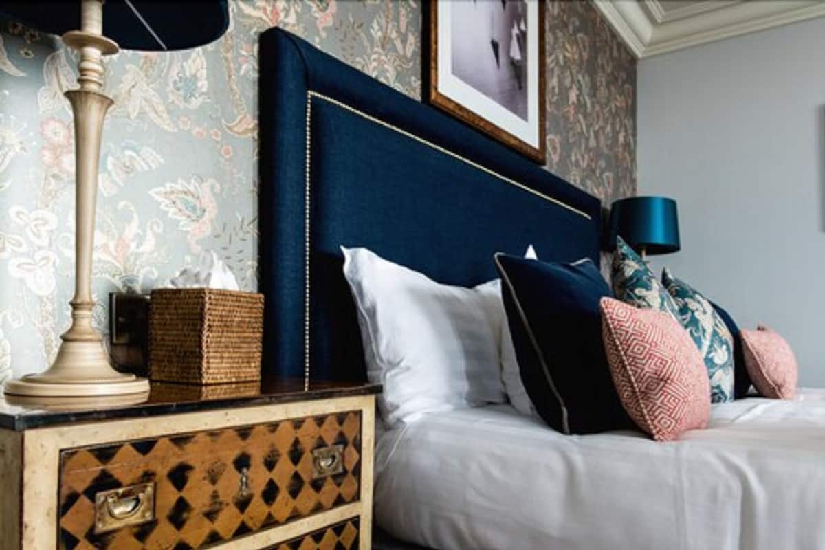 A neatly made bed with a dark headboard, a bedside lamp, and a decorative basket on a dresser with a patterned design.